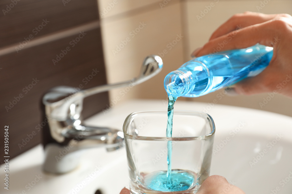 Φωτογραφία Woman pouring mouthwash from bottle into glass in bathroom, closeup