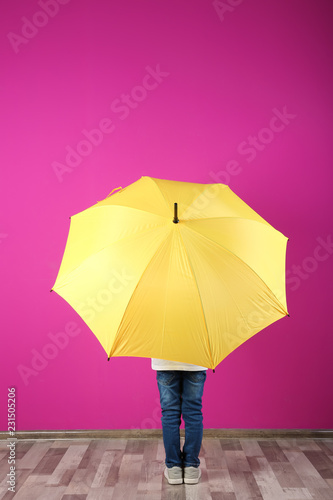 Little boy with yellow umbrella near color wall