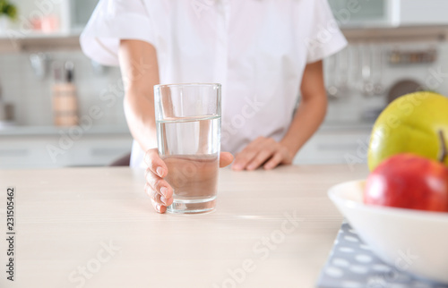 Woman holding glass with clean water on table in kitchen, closeup