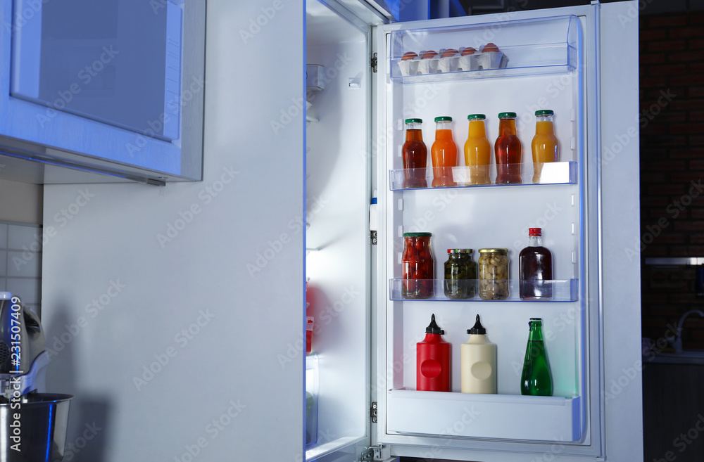 Open refrigerator full of products in stylish kitchen interior at night Open refrigerator full of products in stylish kitchen interior at night