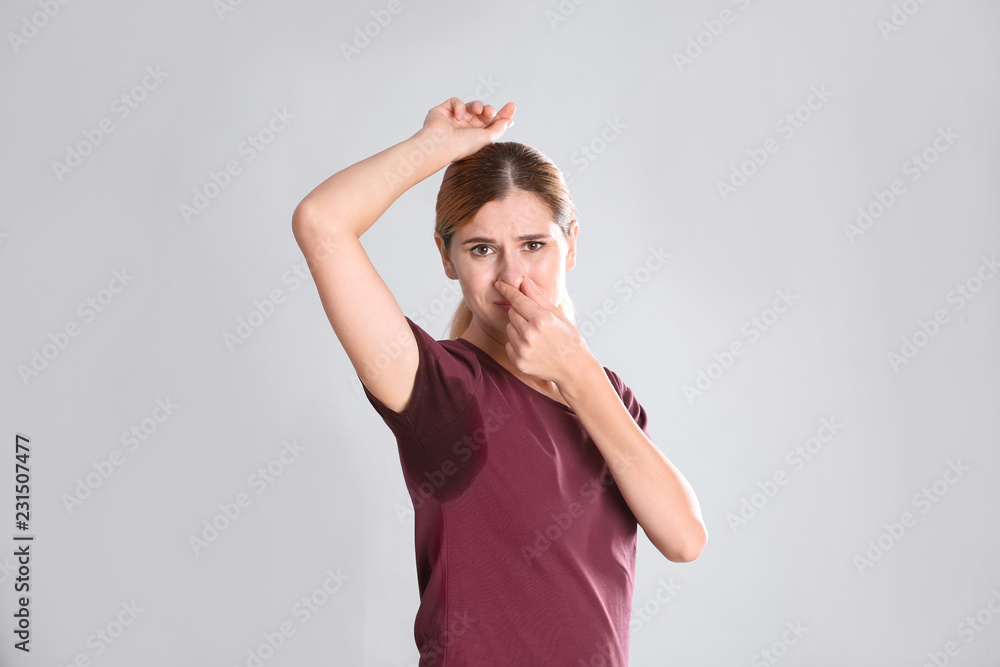 Young woman with sweat stain on her clothes against light background. Using deodorant Young woman with sweat stain on her clothes against light background. Using deodorant