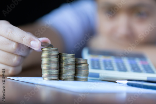 Young happy woman inserting coin on the stacked of coins on desk