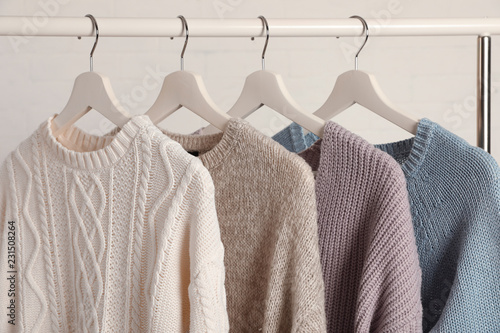 Collection of warm sweaters hanging on rack against white background, closeup