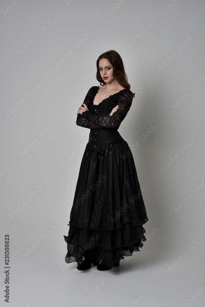 full length portrait of brunette girl wearing long black gown with corset. standing pose on grey studio background. full length portrait of brunette girl wearing long black gown with corset. standing pose on grey studio background.
