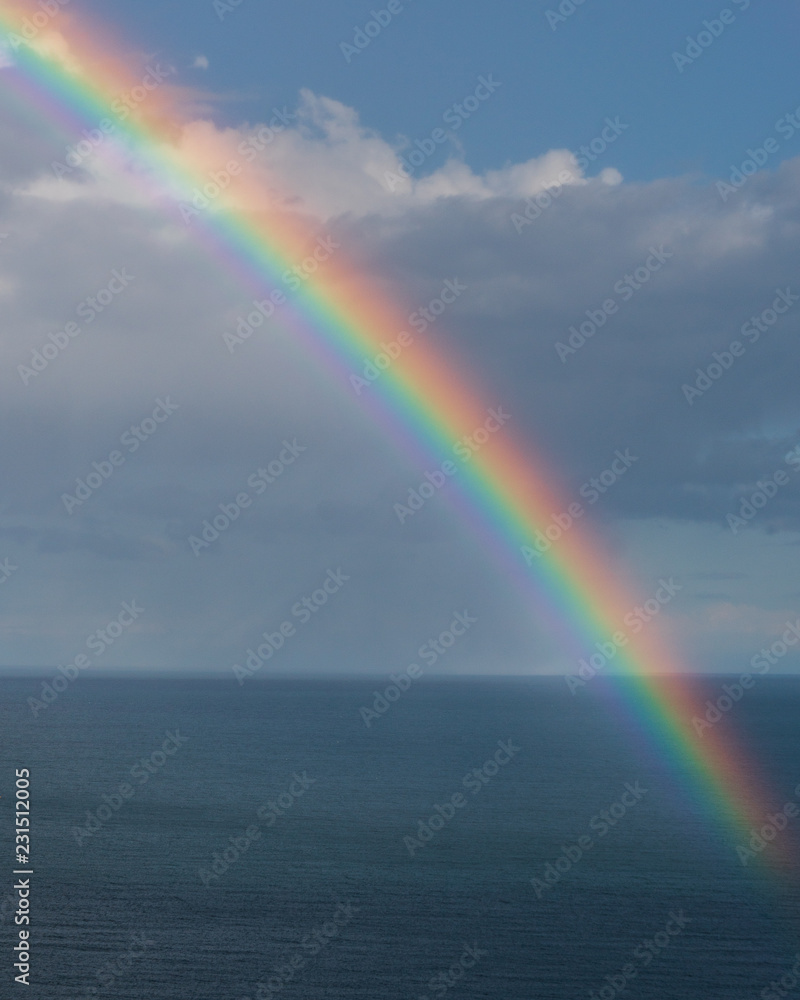 Colourful rainbow over the ocean and a cloudy blue sky background. 