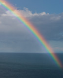 Colourful rainbow over the ocean and a cloudy blue sky background. 