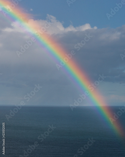 Colourful rainbow over the ocean and a cloudy blue sky background. 