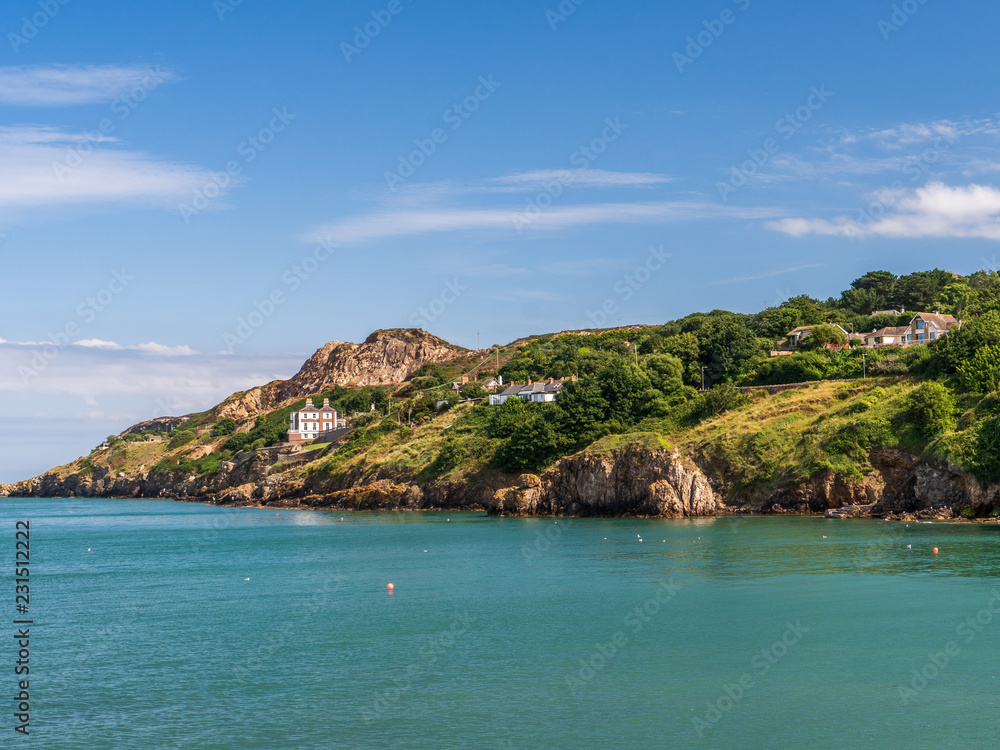 Beautiful Howth coast landscape in Ireland, covered in trees, green and golden grass on a sunny summer day.