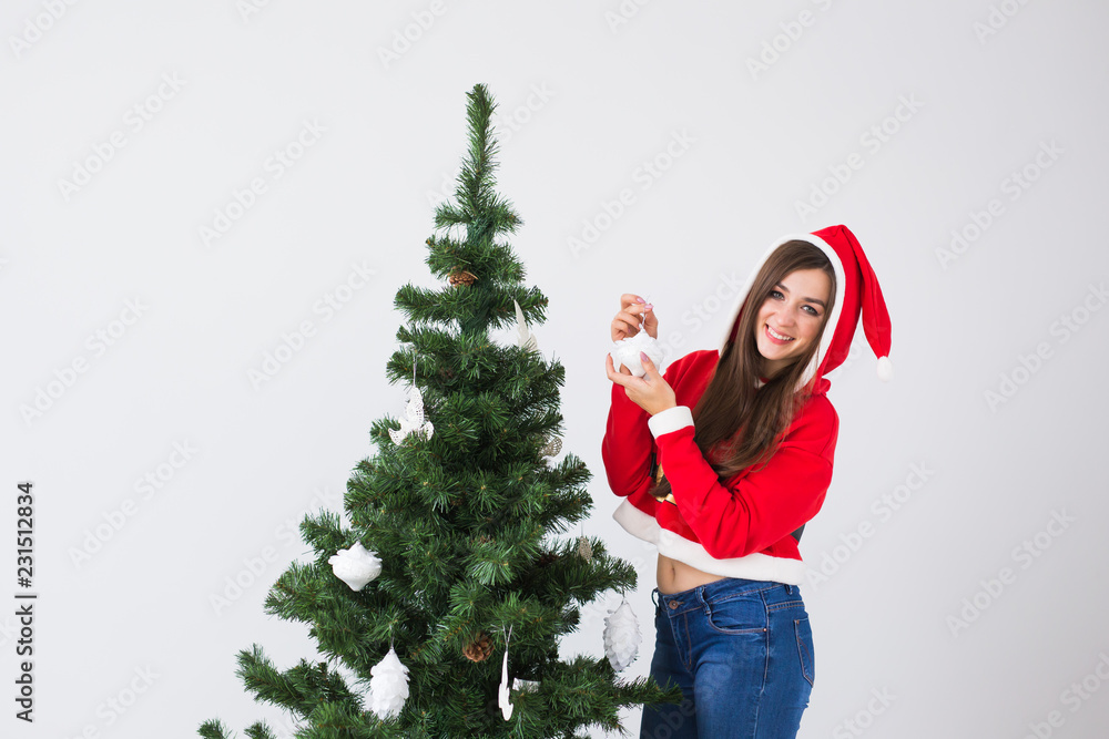 Winter holidays, xmas and people concept - Happy young woman dressed in santa costume decorating Christmas tree in white the room with copy space Winter holidays, xmas and people concept - Happy young woman dressed in santa costume decorating Christmas tree in white the room with copy space