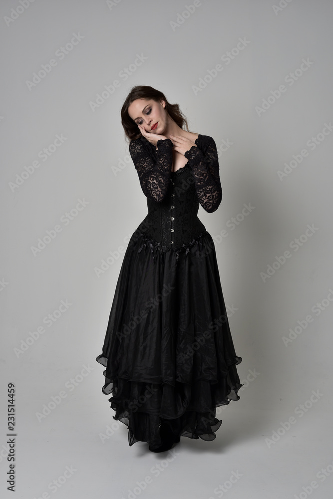 full length portrait of brunette girl wearing long black gown with corset. standing pose on grey studio background. full length portrait of brunette girl wearing long black gown with corset. standing pose on grey studio background.