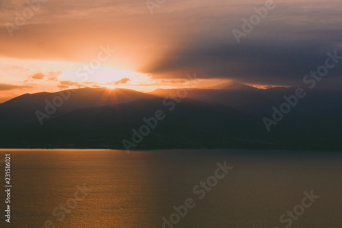 dramatic and atmospheric beautiful mountain sea forest landscape in sun set evening time with rays of light above ridge silhouette horizon shape