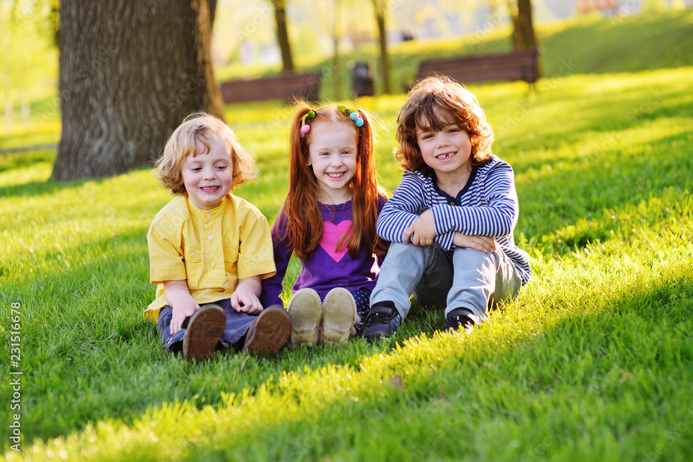 a group of small children in colorful clothes embracing sitting on the grass under a tree in a park laughing and smiling. June 1, Children's Day, vacation, friendship, friends, childhood.