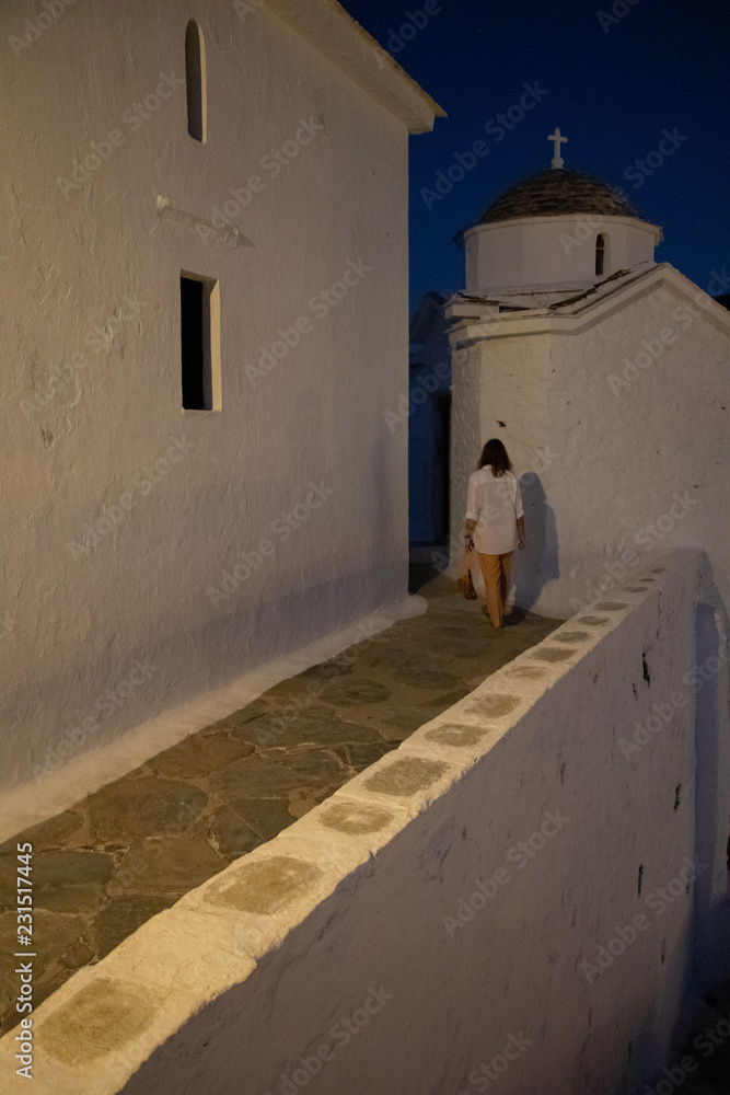 Yong Woman walking by a Typical White Greek Church on the Island Skopelos, Northern Sporades ind the Aegean Sea