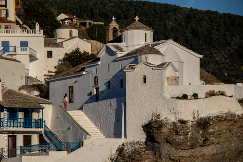Skopelos Old Town, Woman Sightseeing Orthodox Church and small greek houses on the hill as seen from the water on a sailing boat or yacht in the harbor
