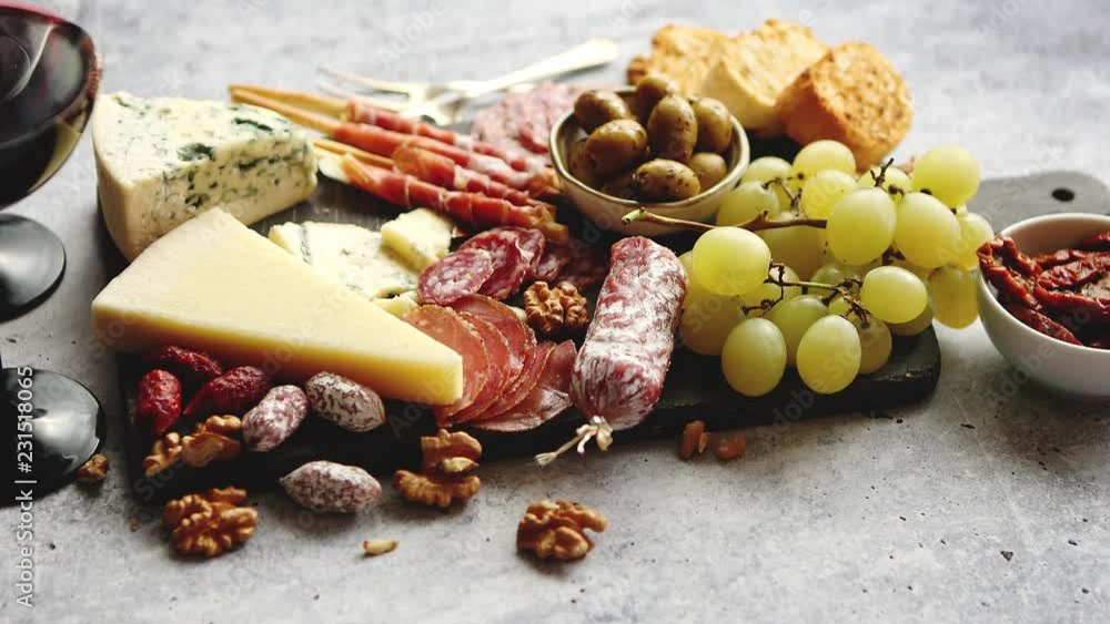 Antipasto platter cold meat and cheese board with grapes, wine, various kinds of cheese, grissini bread sticks on white rustic background. View from above