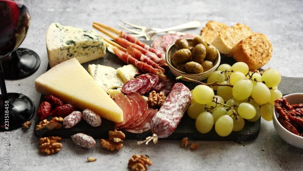Antipasto platter cold meat and cheese board with grapes, wine, various kinds of cheese, grissini bread sticks on white rustic background. View from above