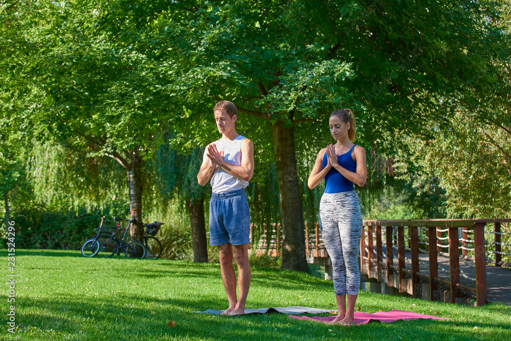 Obraz premium Smiling couple doing yoga exercises outdoors