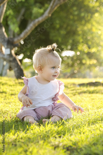 Adorable baby girl on the grass in the park, candid photo with natural back sunlight