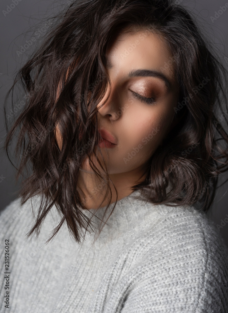 Closeup portrait of a beautiful brunette girl wearing a casual style knitted sweater on gray background. Natural nude makeup. Fashion, advertising and commercial design Closeup portrait of a beautiful brunette girl wearing a casual style knitted sweater on gray background. Natural nude makeup. Fashion, advertising and commercial design
