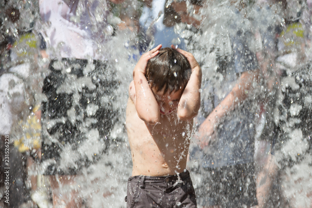 Fototapeta premium Little boy under the water jets. The child bathes in the fountain. Man in the rain.Bathing in the fountain