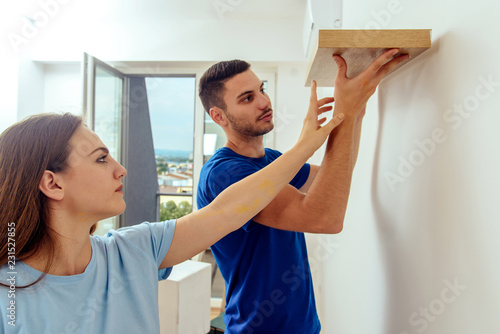 Man hanging shelf on white wall with his girlfriend