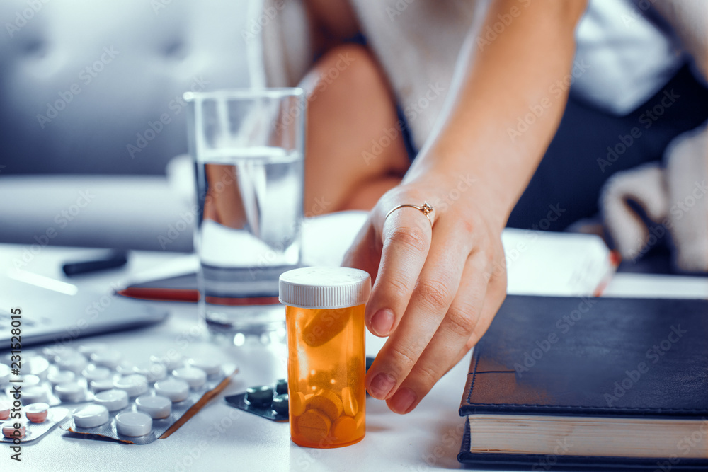 Hand with a ring on the index finger takes the orange container with pills. Other medicines are on the table in blasters. Medical concept. Hand with a ring on the index finger takes the orange container with pills. Other medicines are on the table in blasters. Medical concept.
