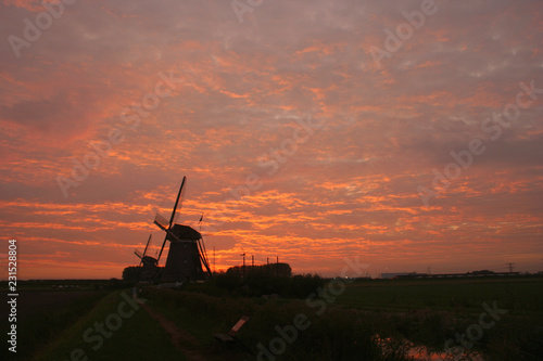 A dutch windmill is silhouetted against a colorful evening sky