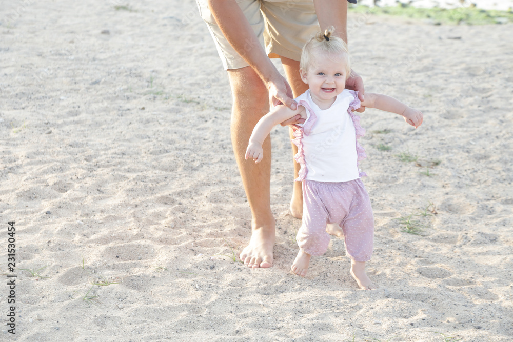 Father helping his baby with the first steps, teaching baby to walk concept, outdoor candid photo on the beach, spending a day at the beach, healthy family lifestyle Father helping his baby with the first steps, teaching baby to walk concept, outdoor candid photo on the beach, spending a day at the beach, healthy family lifestyle