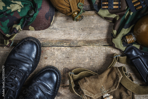 Army military uniform, weapon, holster, pistol, flask, boots on wooden background. Flat lay top view with copy space.Military background