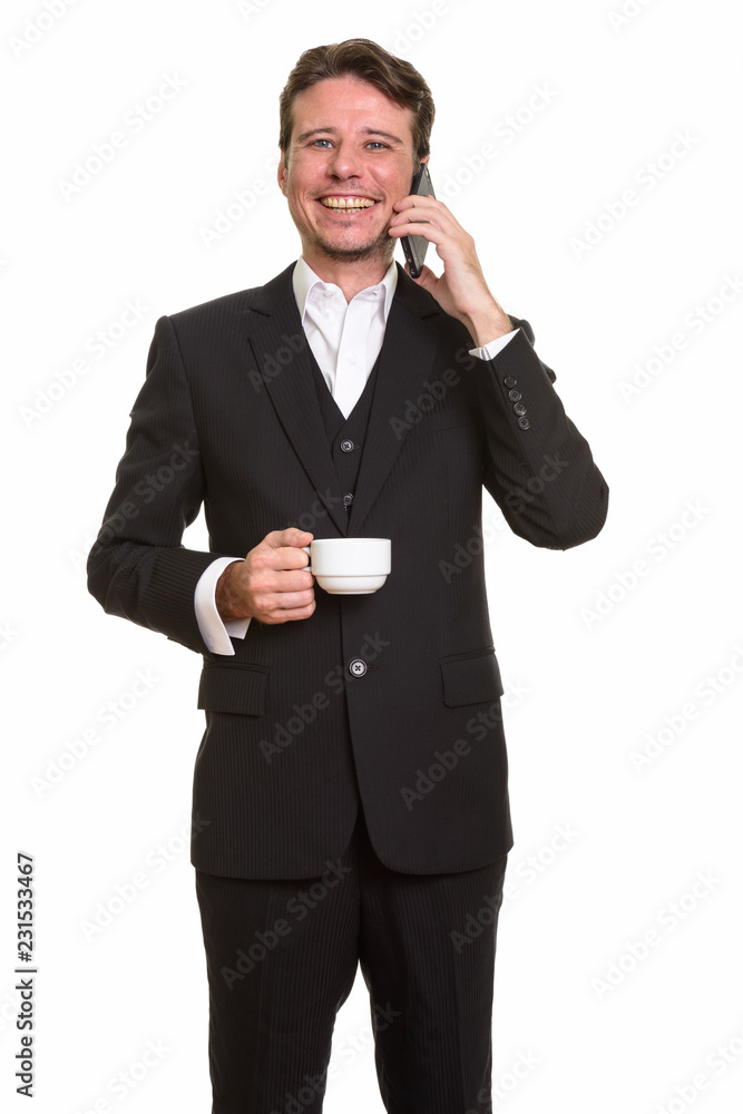 Happy Caucasian businessman talking on mobile phone while holdin Happy Caucasian businessman talking on mobile phone while holdin