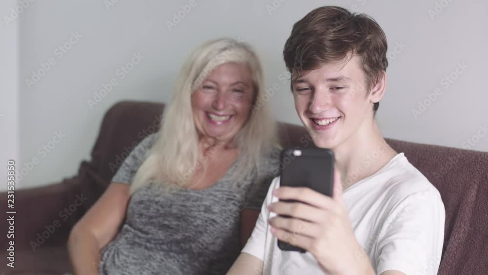 Old grandmother and adult grandson using mobile application on phone tougether seating on the sofa. Doing video call. Happy Family communication concept in 4k. Old grandmother and adult grandson using mobile application on phone tougether seating on the sofa. Doing video call. Happy Family communication concept in 4k.