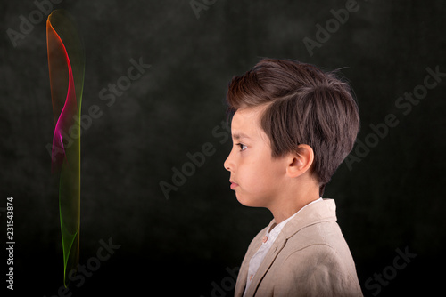 The schoolboy in a beige jacket and with a stylish haircut is standing in profile and looking at a holographic color image or an innovative 3D screen.  Future generation