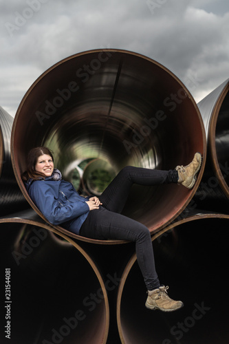 Woman chills in Stacked Oil pipes on a field