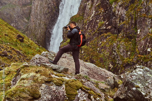 Nature photographer tourist with camera shoots while standing on the mountain against a waterfall.