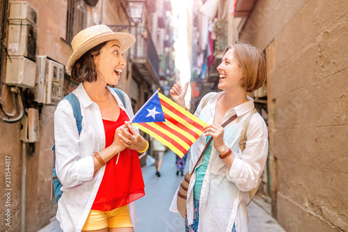 Two Happy woman tourists having fun and travel with catalan flag near the Cathedral in Barcelona city
