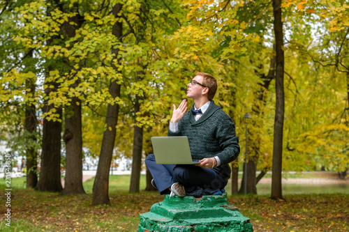 A man with lap top on a pedestal who pretends to be a statue in the the autumn park. Get idea