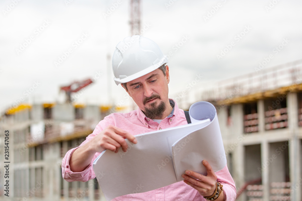 Portrait of architect at work with helmet in a construction site, reads the plan, paper projects
