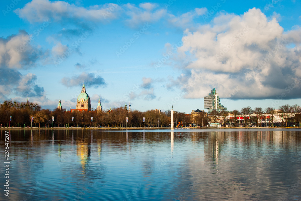 A panorama showing the town hall, a skyscraper, a cloudy blue sky and the lake Maschsee in Hanover, Germany