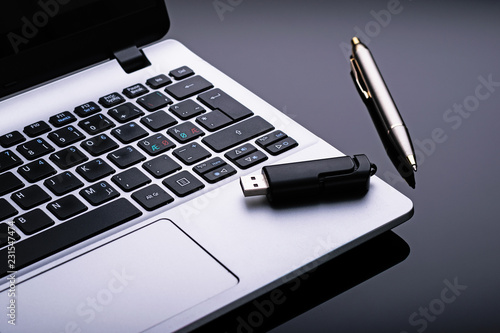 Laptop with pen and usb flash memory on dark background.