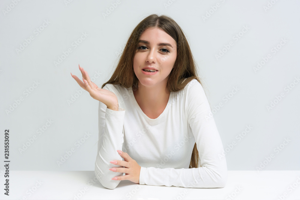 Studio portrait of a smiling happy beautiful brunette girl on a white background talking and sitting at the table. Studio portrait of a smiling happy beautiful brunette girl on a white background talking and sitting at the table.