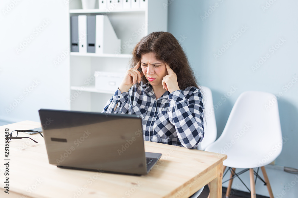 Fototapeta premium Young woman has a headache while working on laptop in office