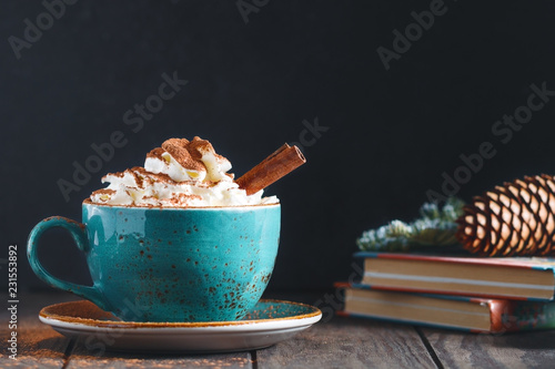 фотографія Hot chocolate with cream and cinnamon stick in a blue ceramic cup on a table with a books
