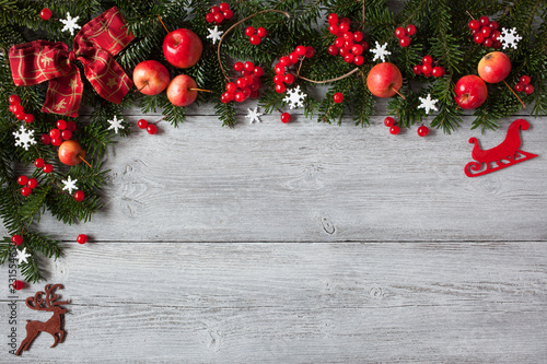 Christmas wooden background with fir branches, snowflakes, red apples and berries