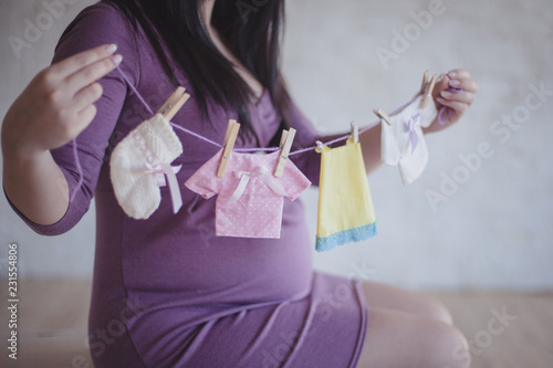 Pregnant woman holds a rope with tiny baby clothes hanging on it