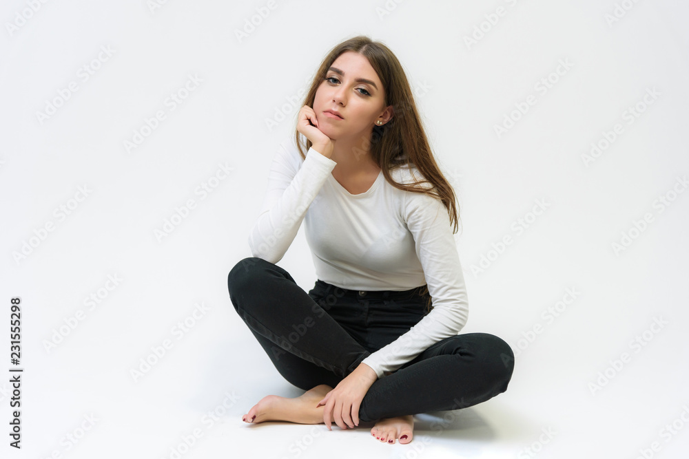 Studio portrait of a smiling happy beautiful brunette girl on a white background talking and sitting on the floor. Studio portrait of a smiling happy beautiful brunette girl on a white background talking and sitting on the floor.