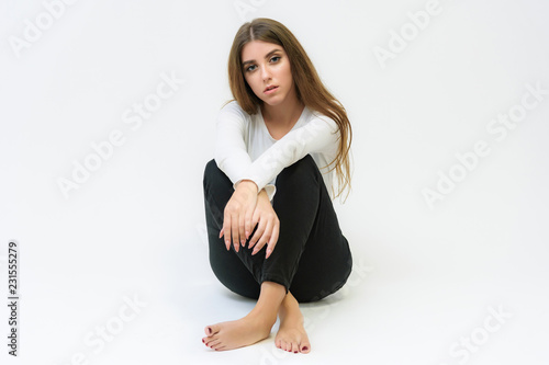 Studio portrait of a smiling happy beautiful brunette girl on a white background talking and sitting on the floor.