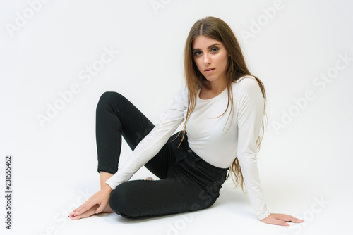 Studio portrait of a smiling happy beautiful brunette girl on a white background talking and sitting on the floor.