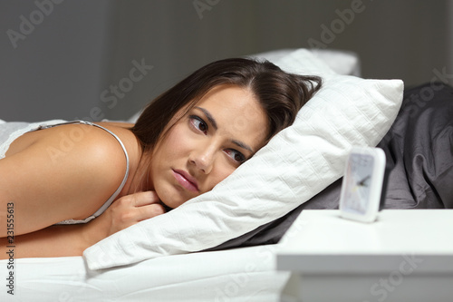 Sleepless insomniac girl looking at alarm clock in the night