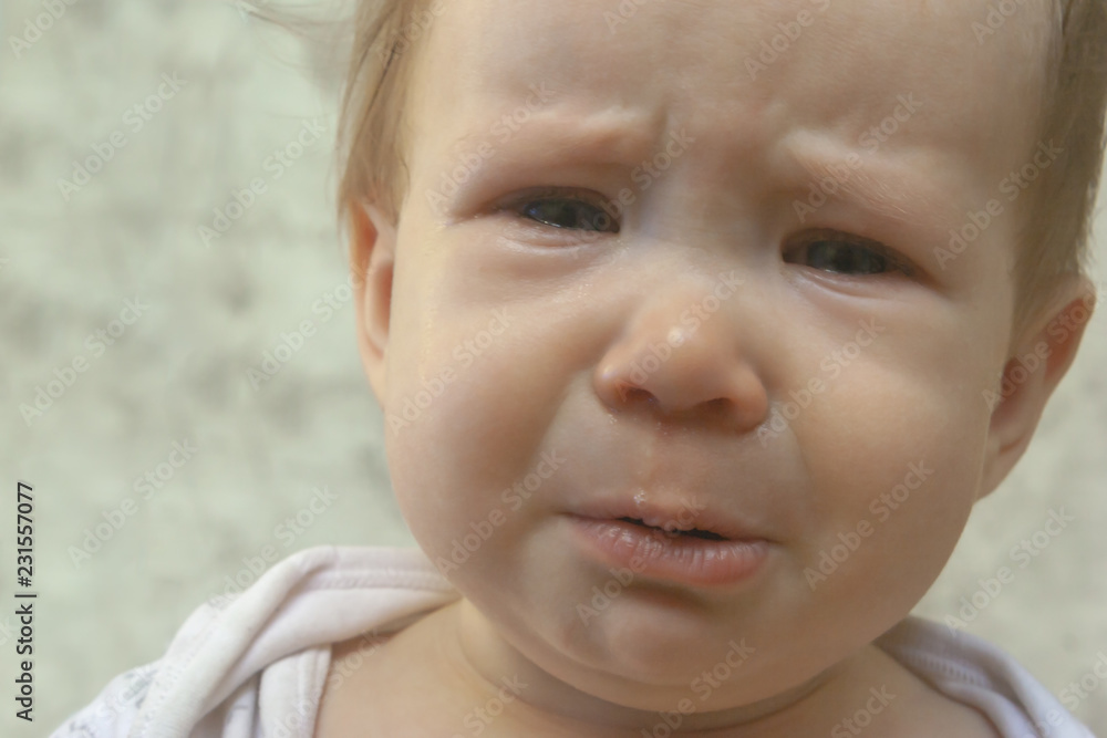 A sad, crying child purses his lips and sheds tears. Portrait in beige tones A sad, crying child purses his lips and sheds tears. Portrait in beige tones
