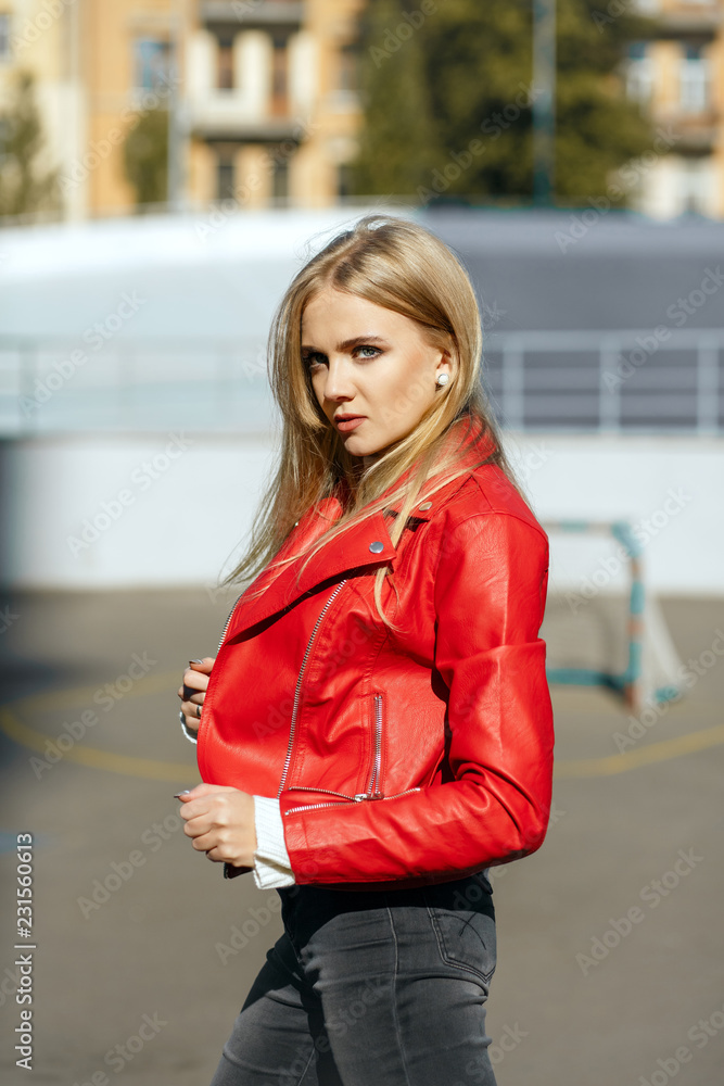 Wonderful blonde girl with long hair wearing red leather jacket posing in  sun light Stock Photo | Adobe Stock